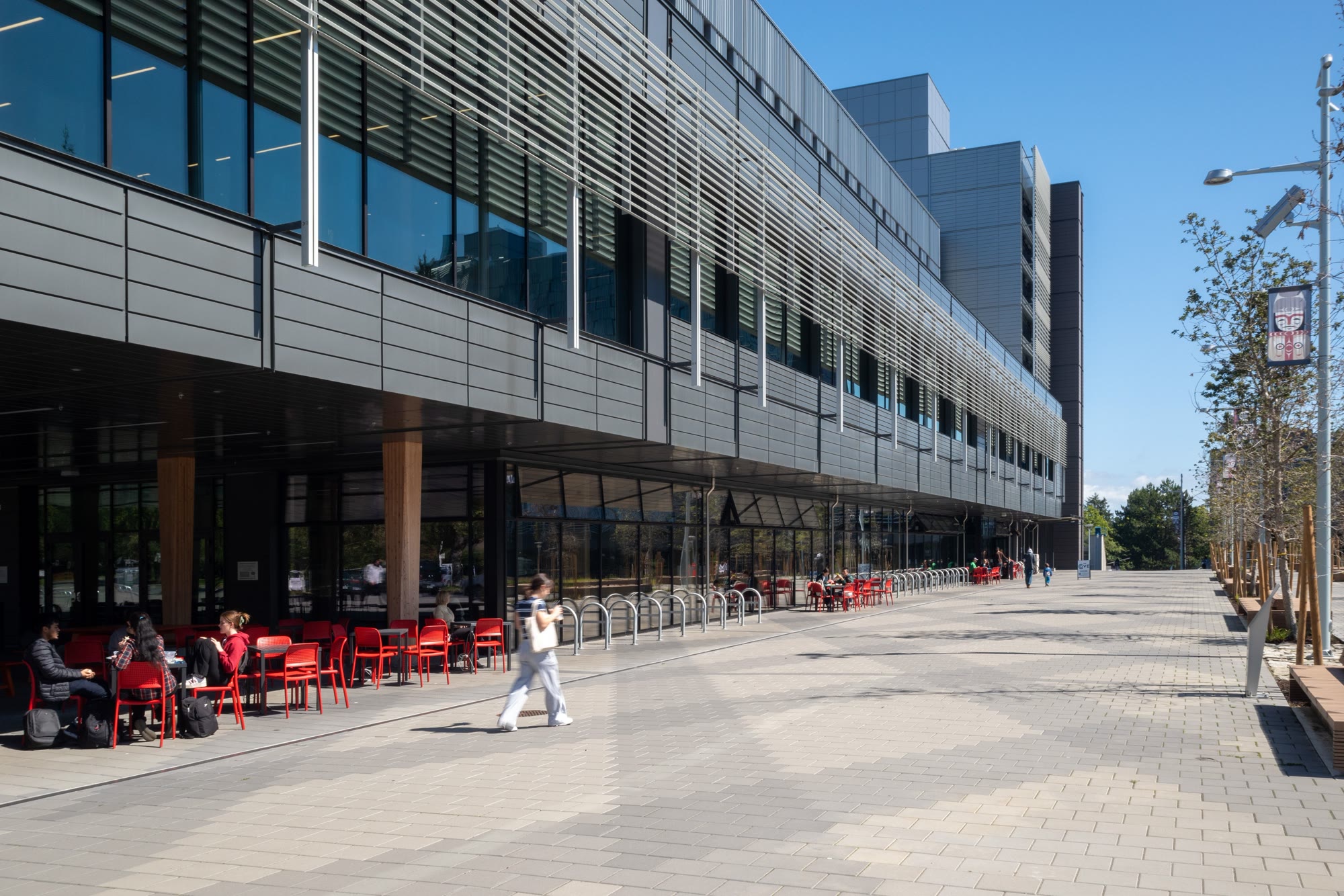Students at café tables outside one of the University of Victoria's newer buildings on a sunny day