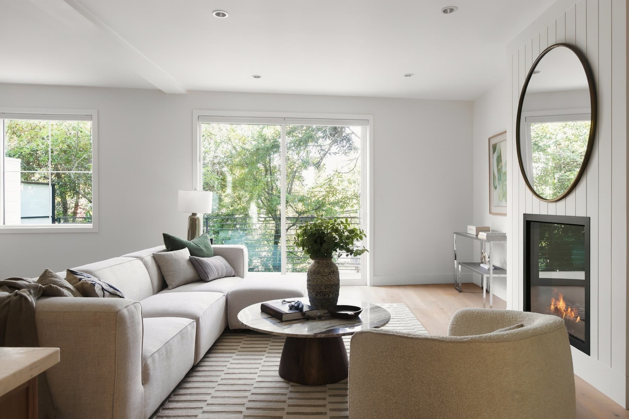 The living room, with a sectional sofa, a round coffee table and the fireplace under a round mirror