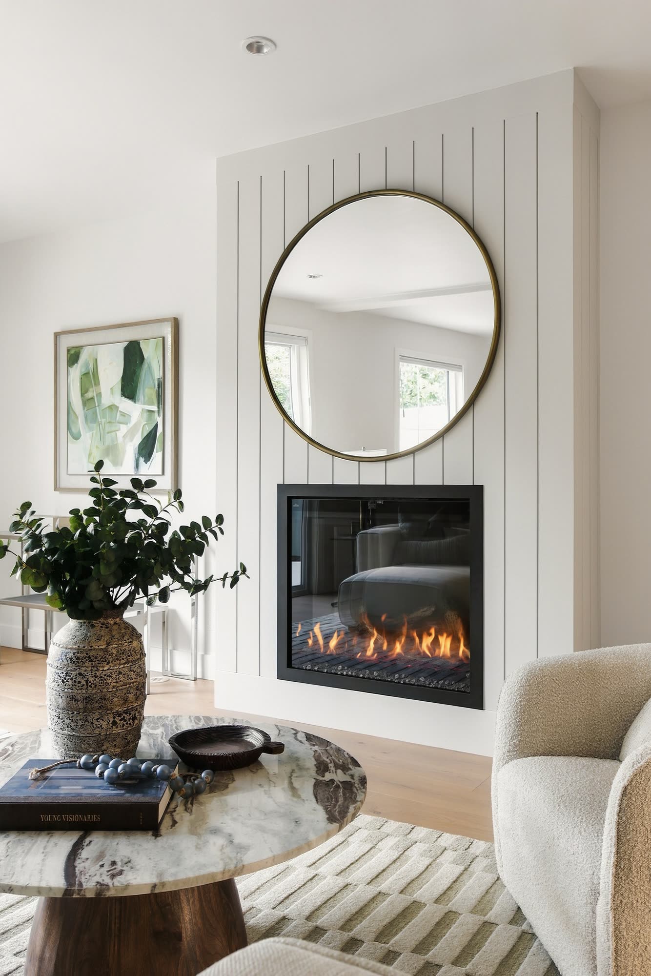 The fireplace in a white panelled wall, with a round brass mirror above