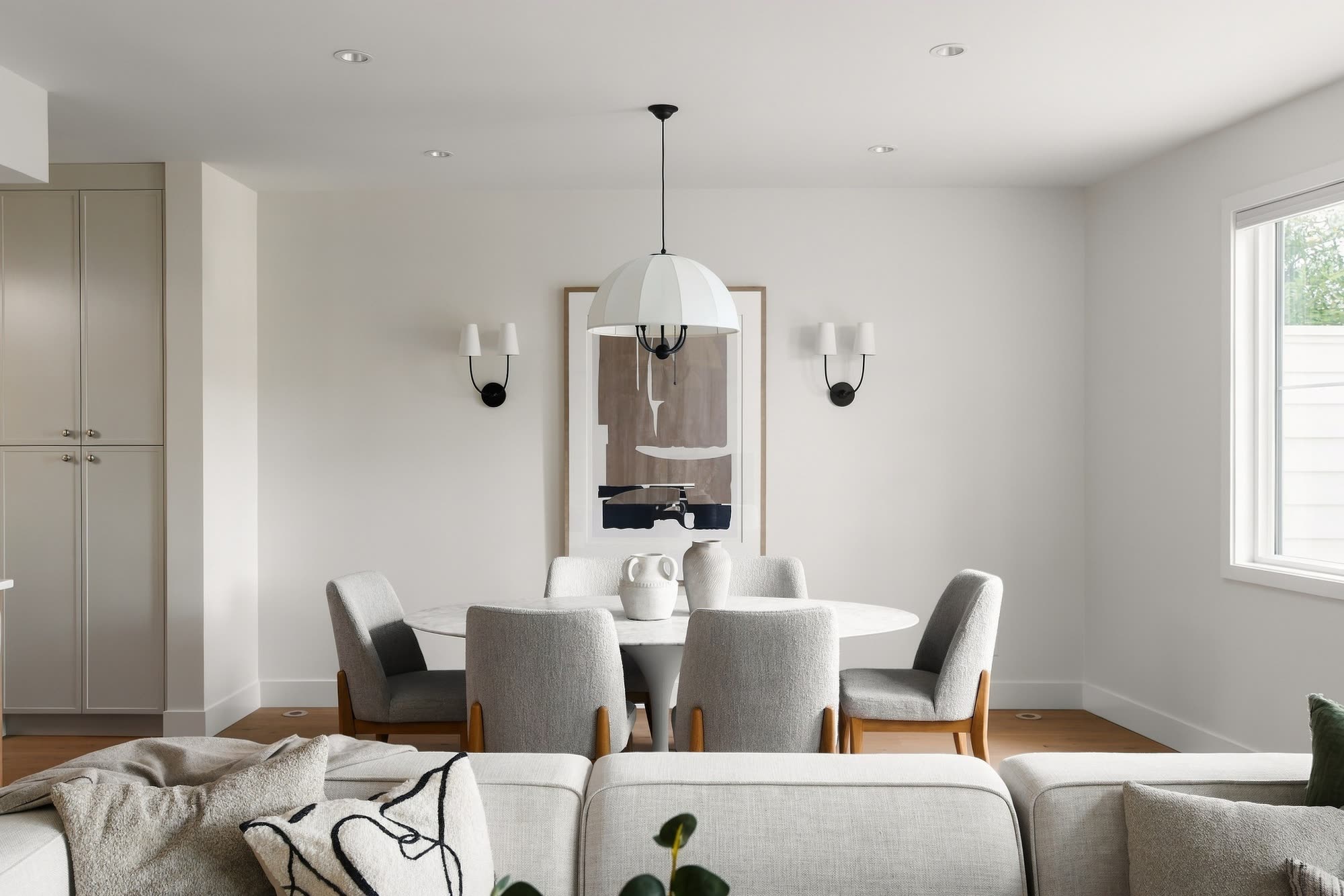 The dining table under a pleated pendant, with the kitchen behind