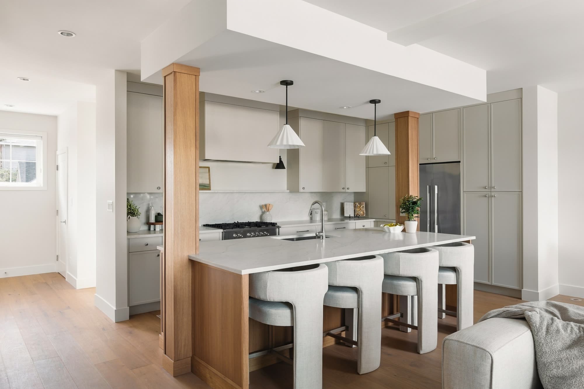 The Home 1 kitchen: oak columns, a long quartz island with white stools, and cone pendants