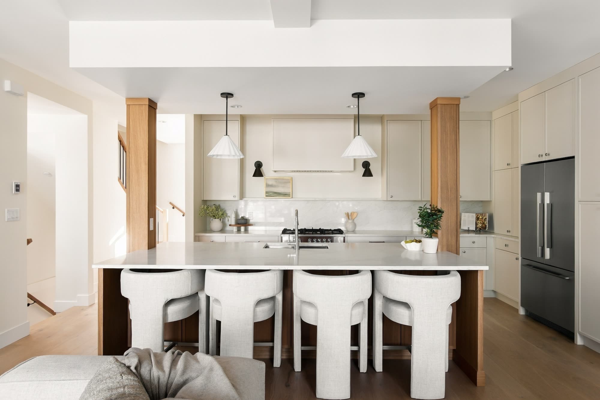 The kitchen straight on: a long quartz island with four stools between two oak columns