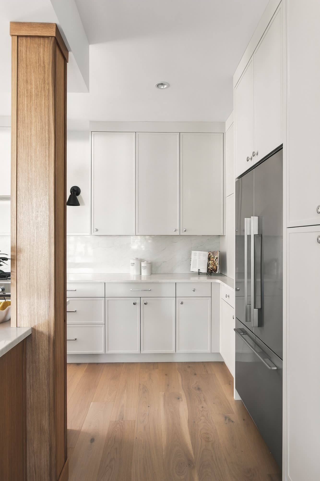 The fridge wall and tall cabinets beside an oak column
