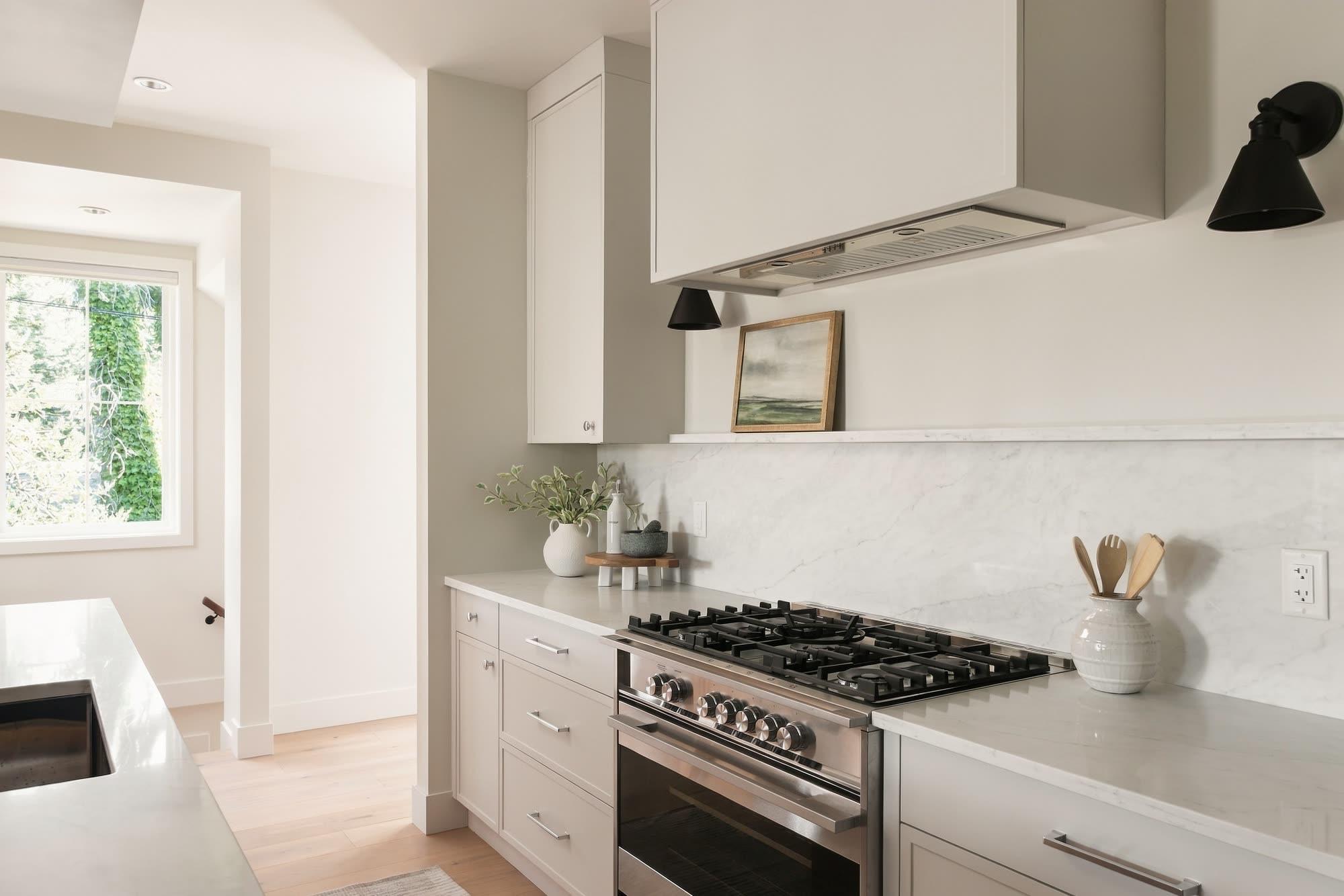 The gas range under a white hood, with quartz counters and shaker cabinets