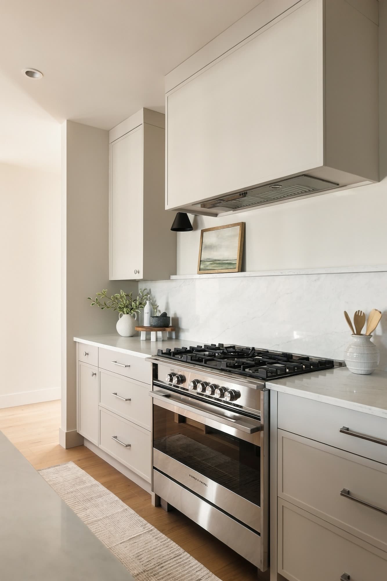 The range wall: a gas range under a white hood, with quartz counters and shaker cabinets