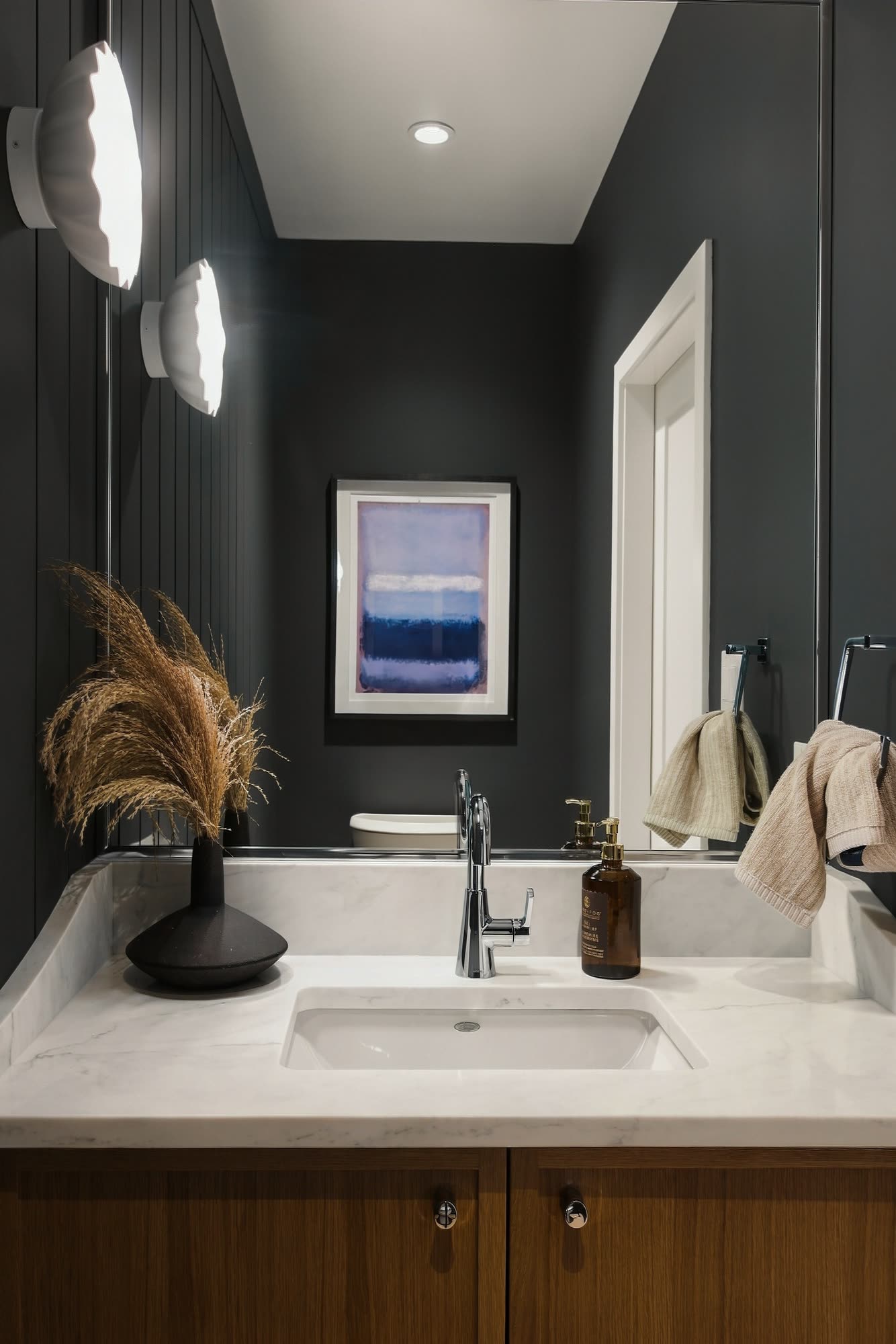 The powder room, with dark walls, globe lights and an oak vanity