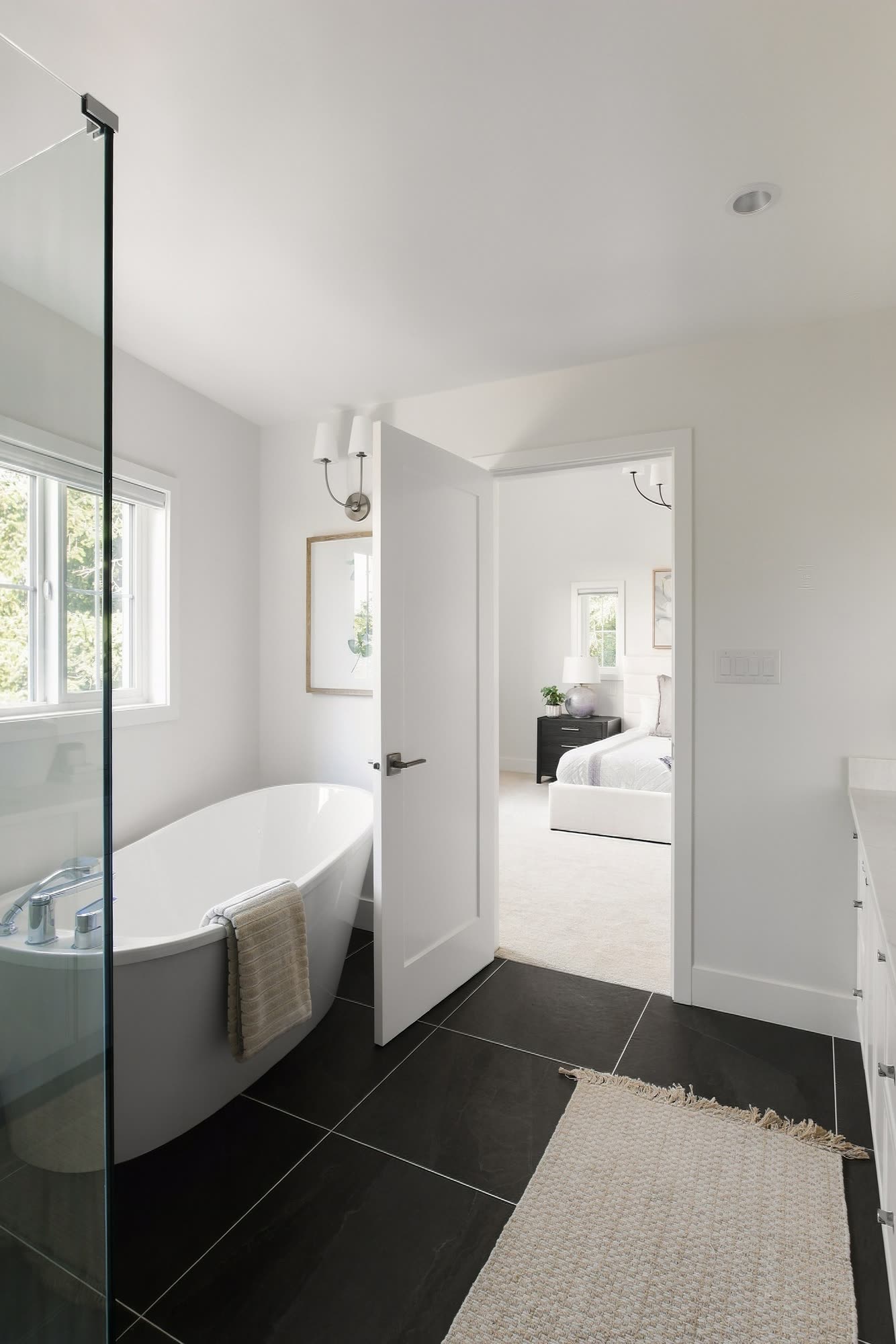 The ensuite's freestanding tub by the window, on black floor tile