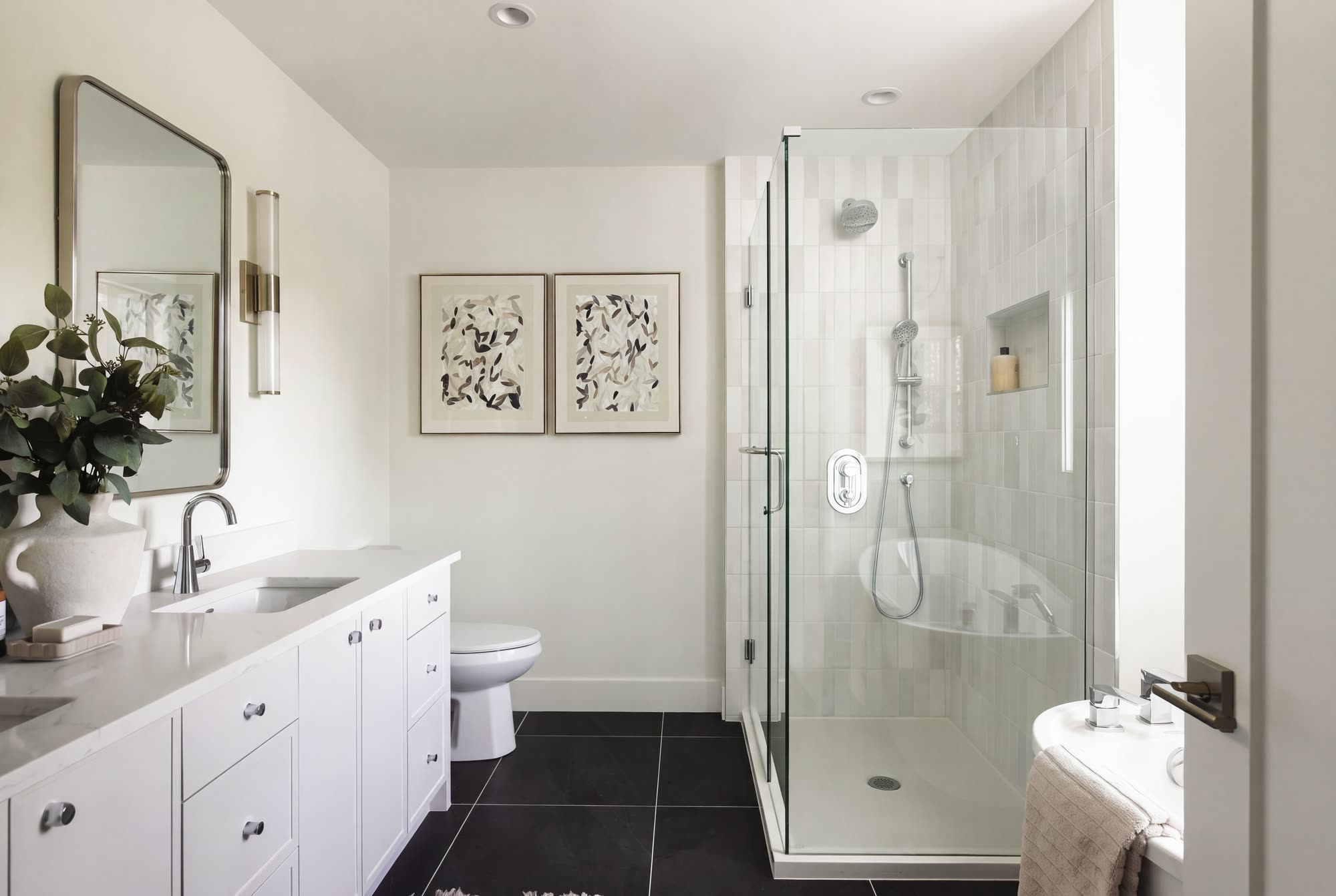 The ensuite, with a white vanity, a glass shower and black floor tile