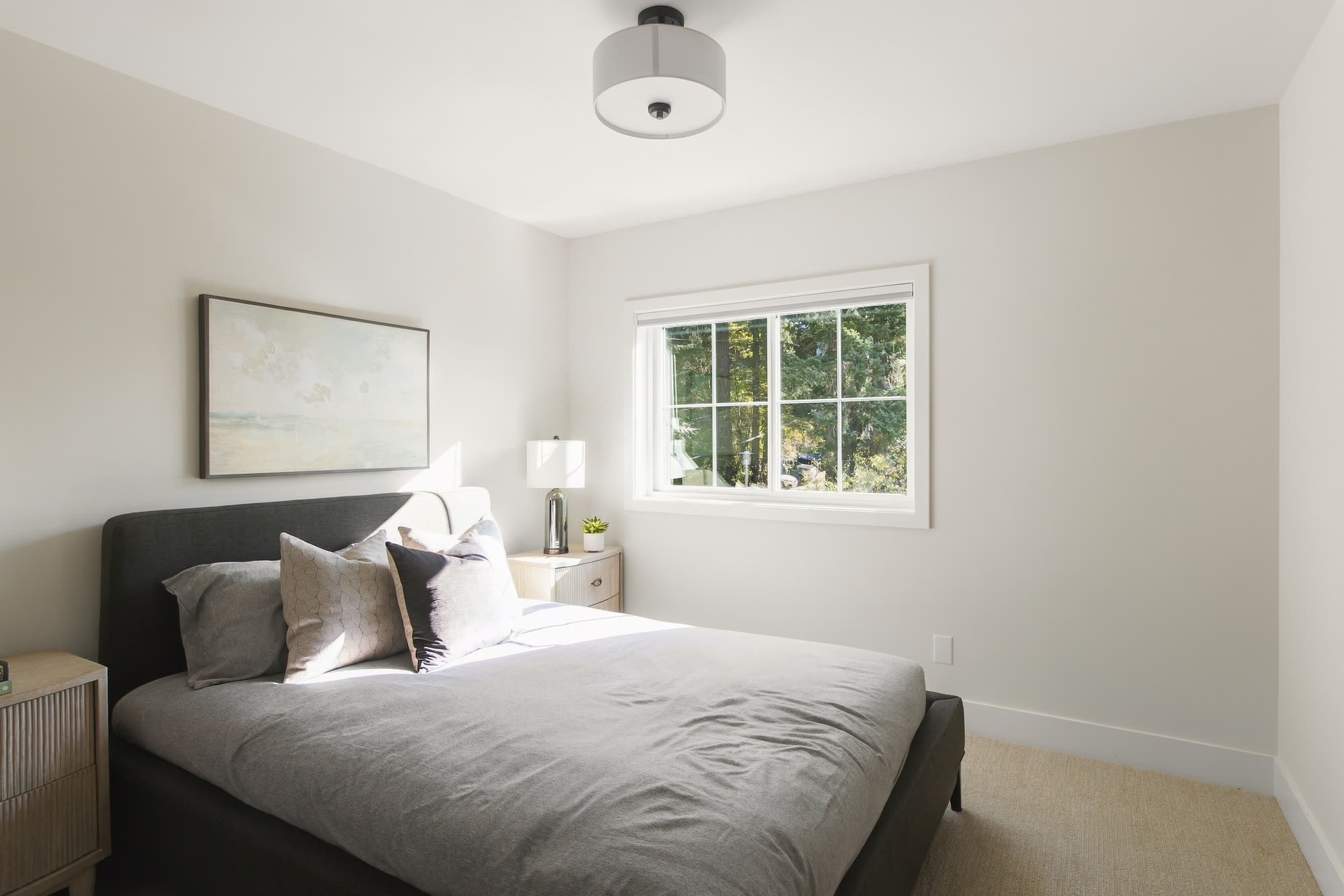 A bedroom with a grey upholstered bed and a window