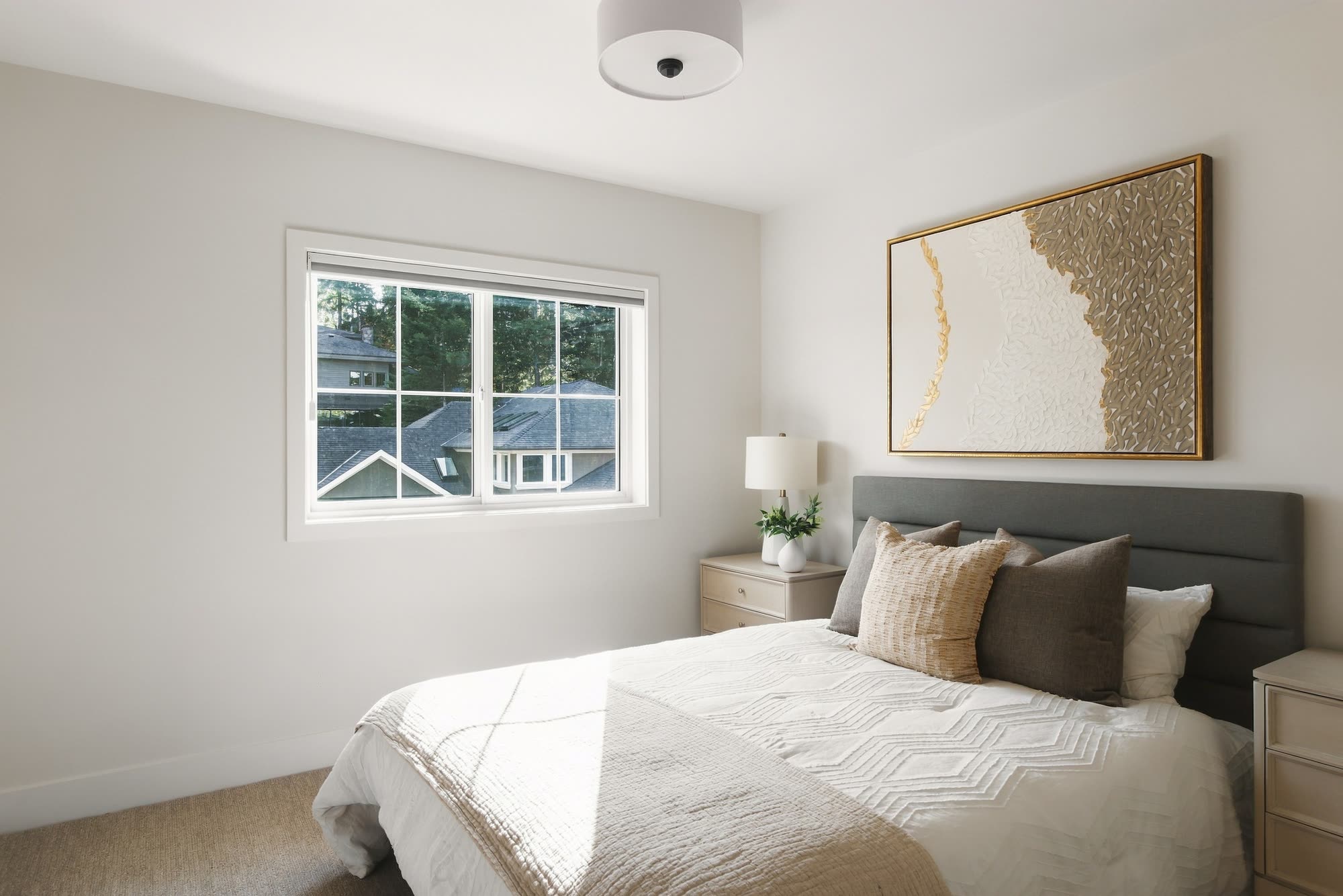 A bedroom with a grey headboard, gold artwork and a window